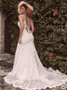 Woman looks over shoulder in white wedding dress in front of wall of vines
